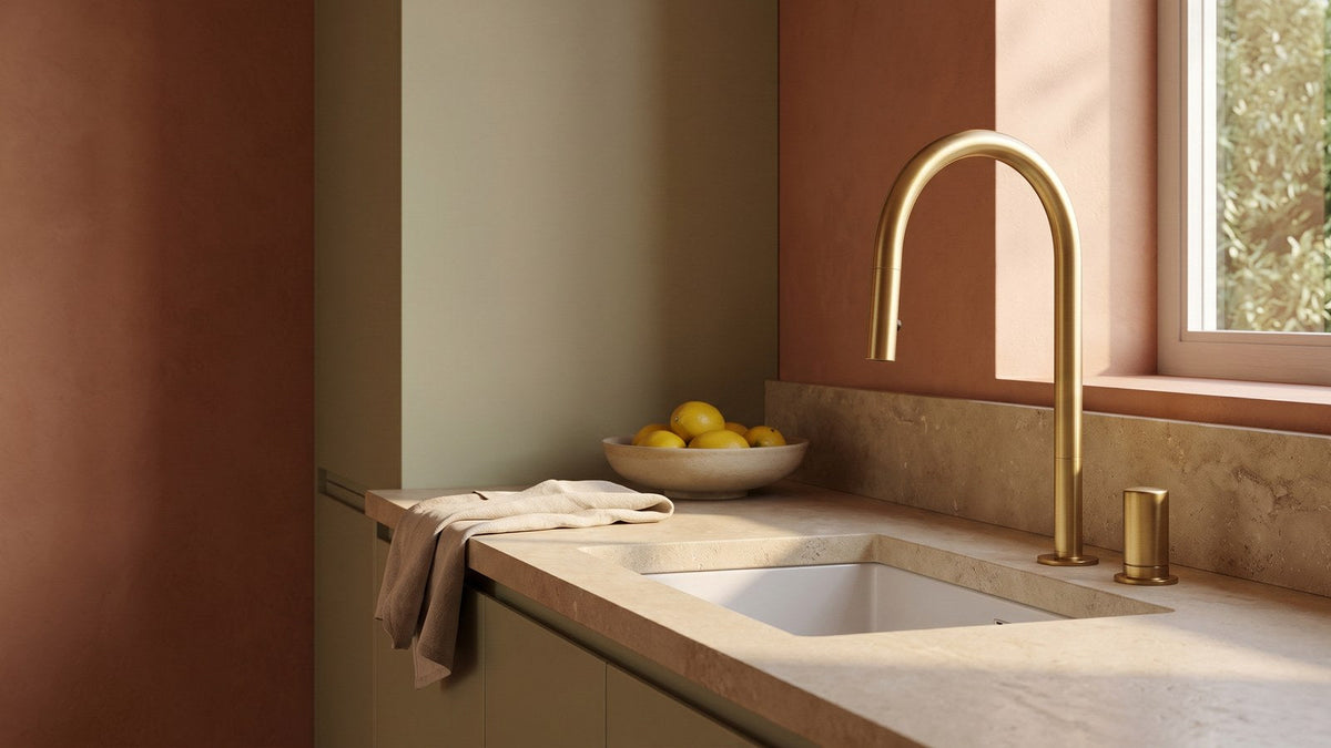 Brushed gold 2 hole kitchen faucet on a limestone counter, the gooseneck spout in one hole and its plain cylindrical mixer control in the second