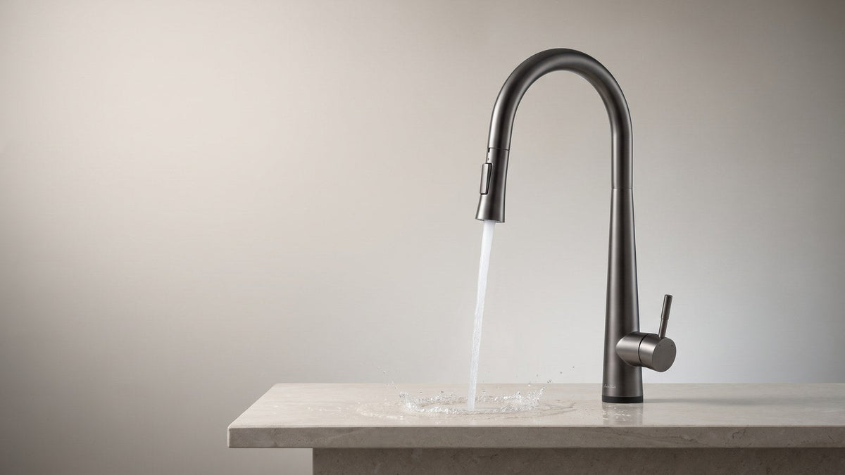 Gunmetal gray touch kitchen faucet running a clear stream of water onto a pale stone countertop