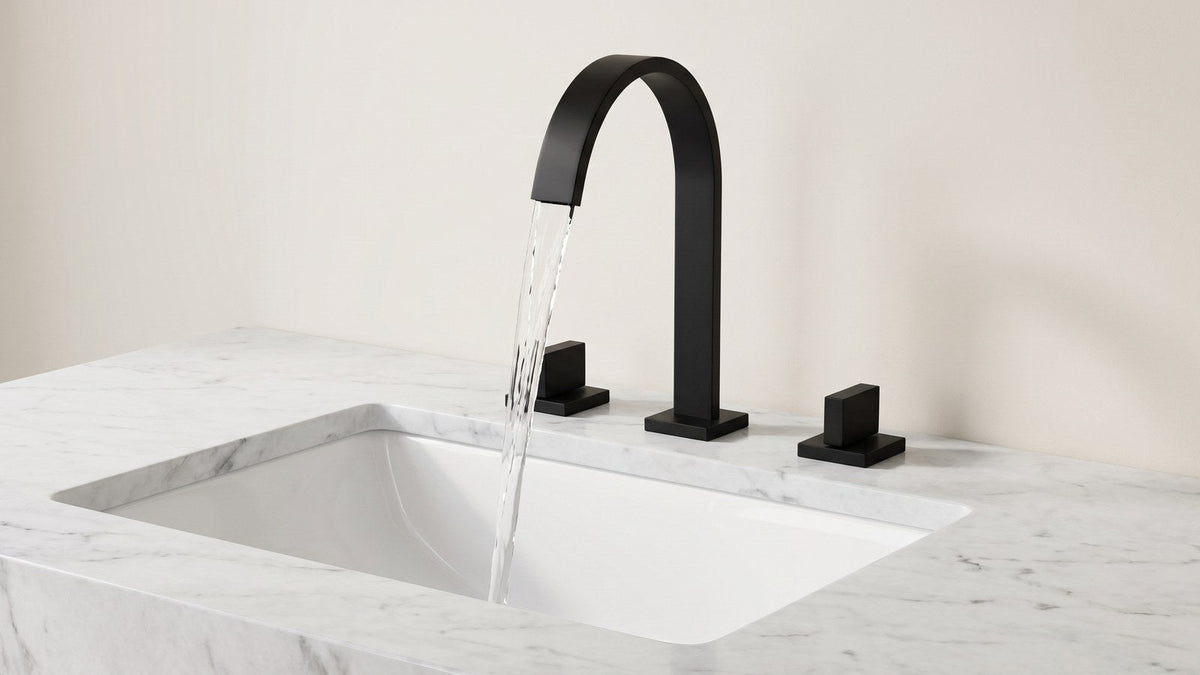 Matte black Freyer widespread waterfall faucet on a white marble vanity, water leaving the open spout channel as a flat sheet into a deep rectangular basin