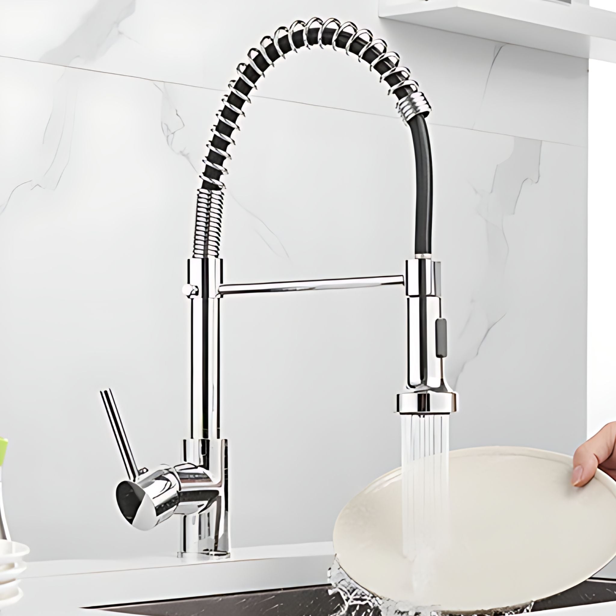 A modern pull-down kitchen faucet with a flexible coiled hose and chrome finish, shown installed in a sink with water running while a hand holds a plate under the stream. #color_chrome