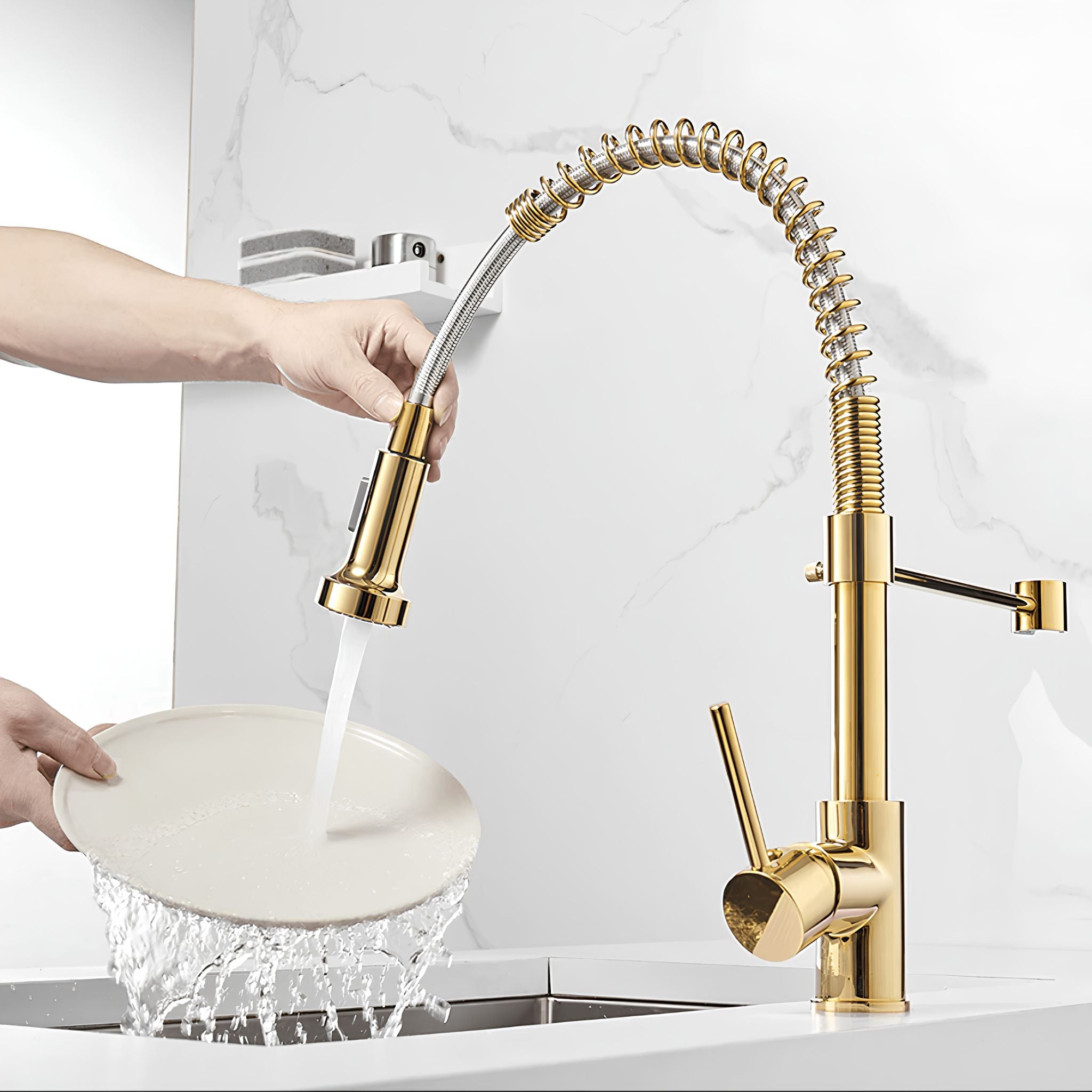 A high-arc gold pull-down kitchen faucet with a flexible spring coil neck, shown with a person's hands running water from the spray head into a white plate over a sink. #color_gold