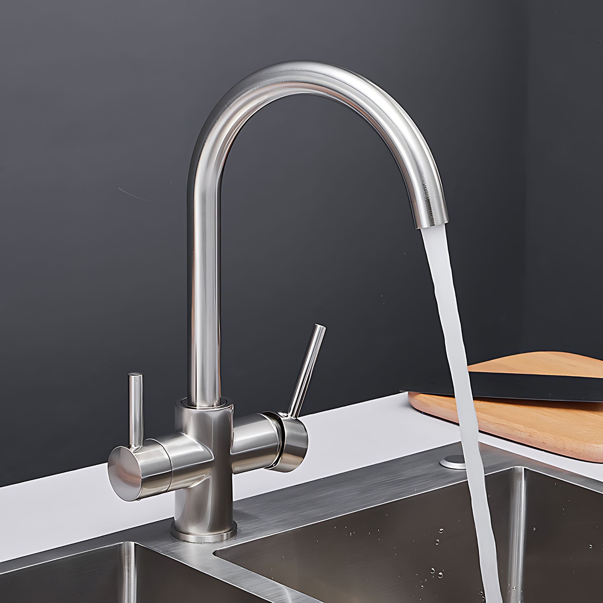 A modern dual-handle kitchen faucet with a high-arc spout and side lever, shown with water running into a stainless steel sink. The faucet has a brushed silver finish and is set against a dark gray background with a wooden cutting board on the counter. #color_brushed nickel