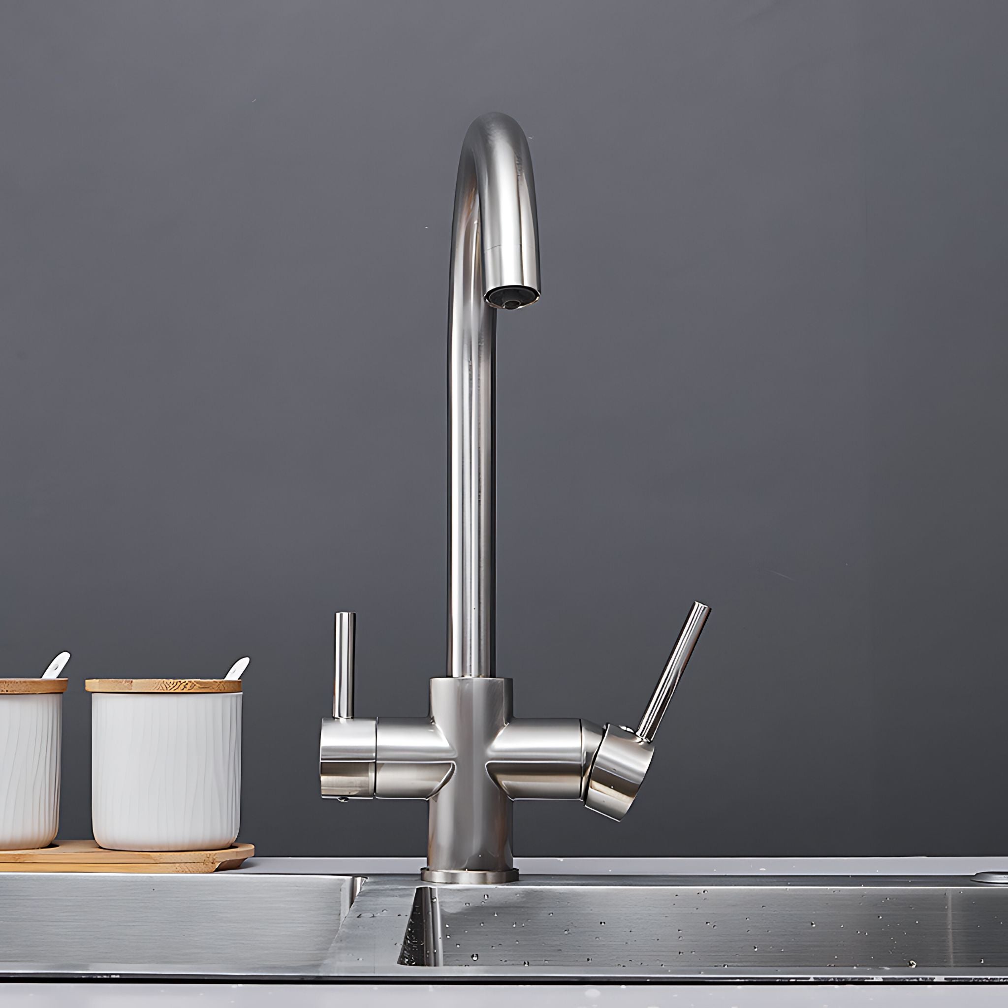A modern stainless steel kitchen faucet with a high-arc spout and dual lever handles, installed on a metal sink against a dark gray background. #color_brushed nickel