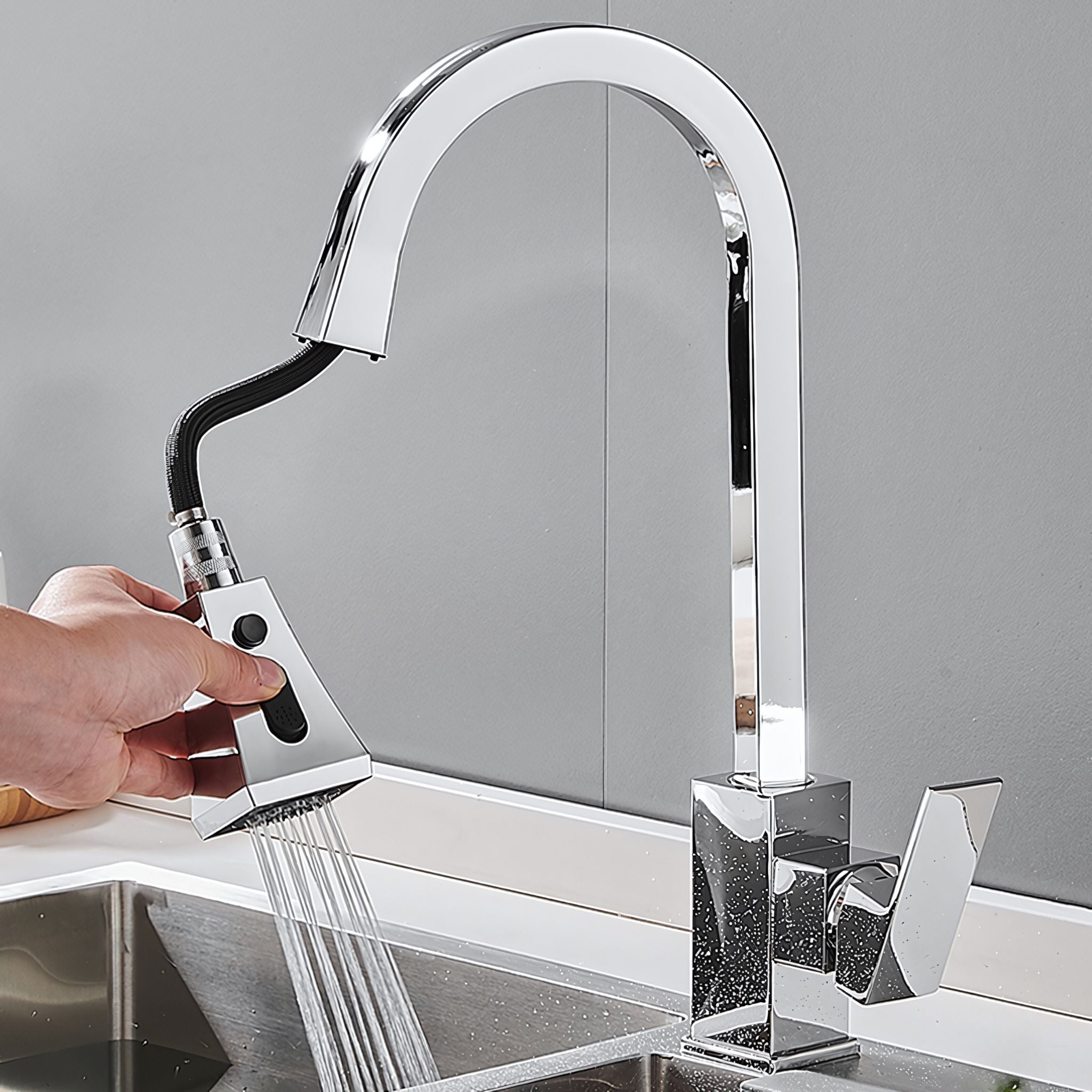 A modern high-arc chrome pull-down kitchen faucet with a hand holding the detachable spray head under running water in a stainless steel sink. #color_chrome