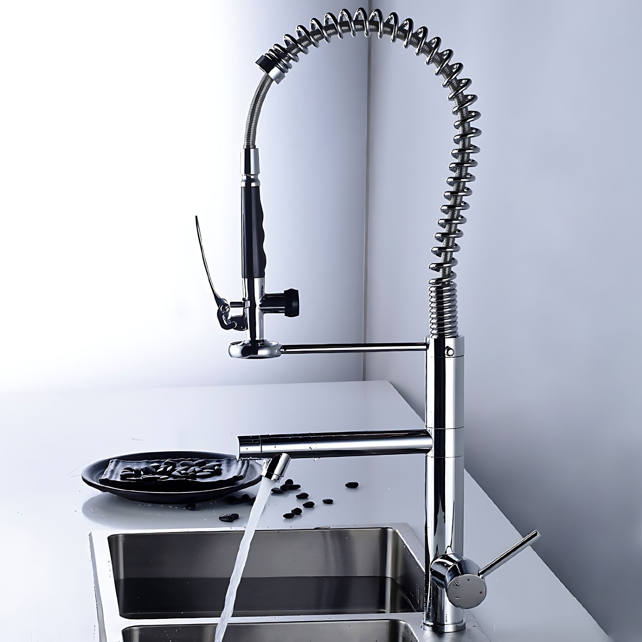 A modern stainless steel pull-down kitchen faucet with a flexible coiled spout, shown installed over a double-bowl sink with water running. The faucet has a polished chrome finish with black accents on the handle and side lever, set against a clean white and light gray background. #color_chrome