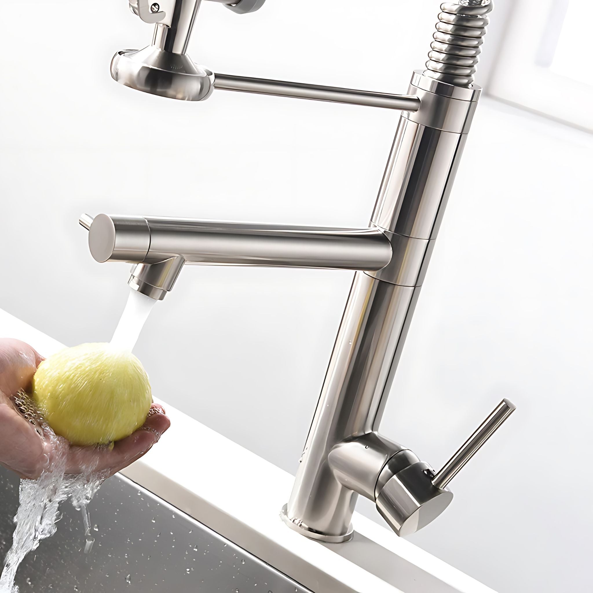 A modern stainless steel kitchen faucet with a high-arc spout, a side lever handle, and a flexible pull-down sprayer, shown with water running into a sink while a hand holds a yellow sponge under the stream. #color_brushed nickel